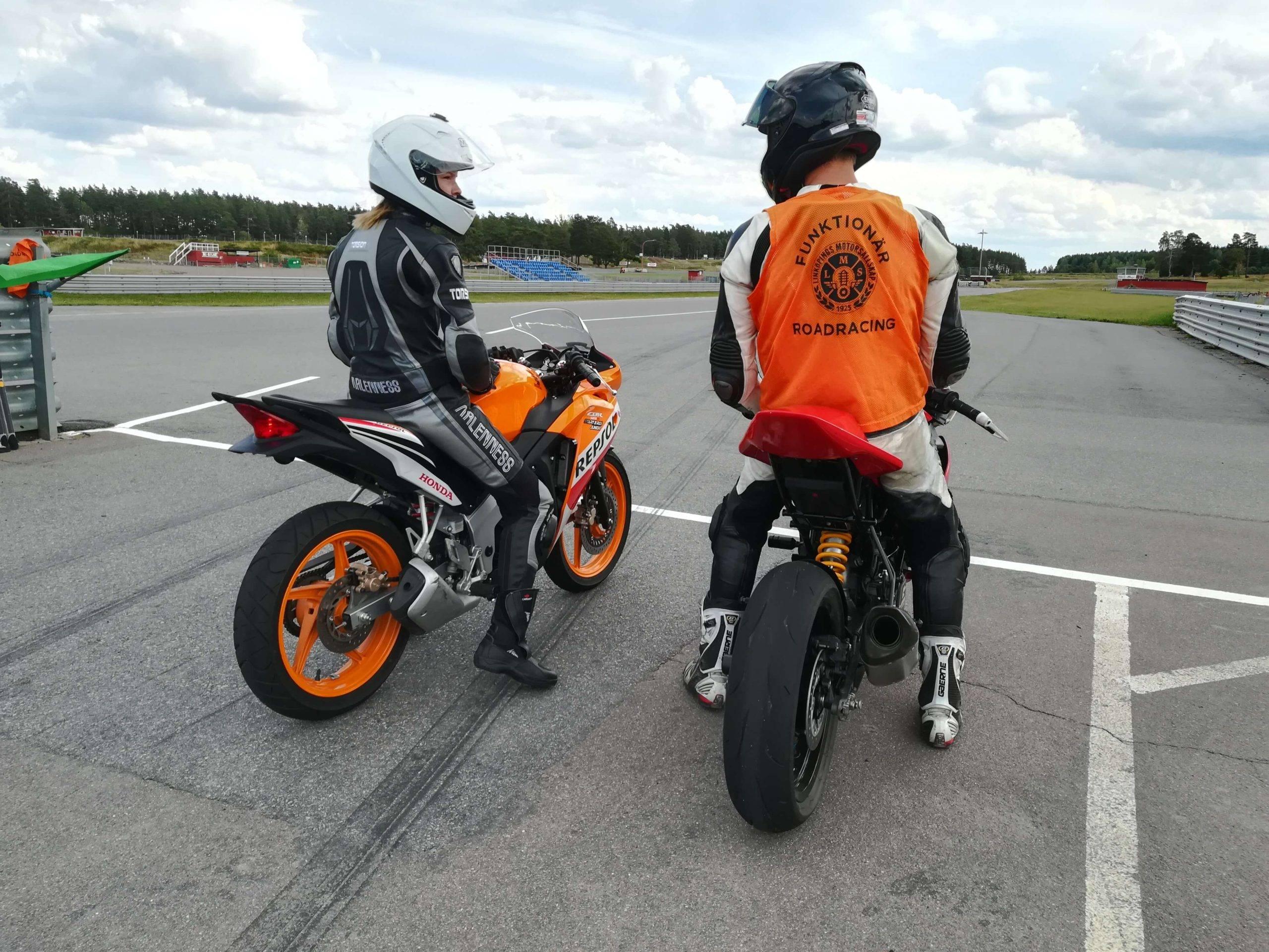 Två förare på varsinn roadracinghoj står brevid varandra vid starten på banan och diskuterar.