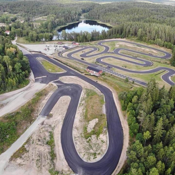 En drönarbild på en stor anläggning med asfaltbana i en skog bredvid en sjö
