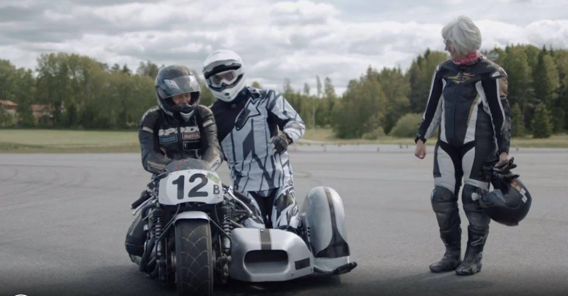 En förare på sin mc och en burkslav i sidovagnen i Classic roadracing. En annan förare står bredvid och ler.