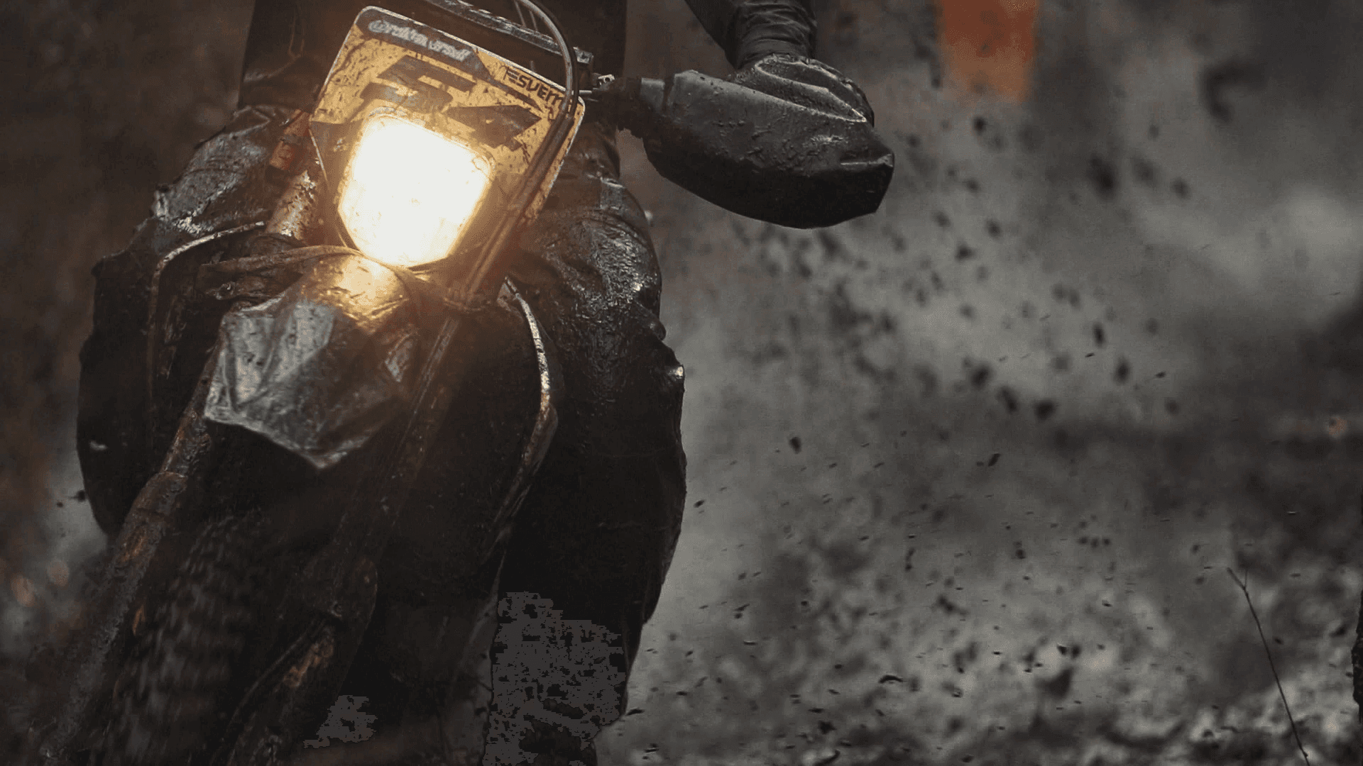 En väldigt lerig enduro med förare i ett mörkt och gyttjigt landskap. Lampan på enduron lyser upp spåret.