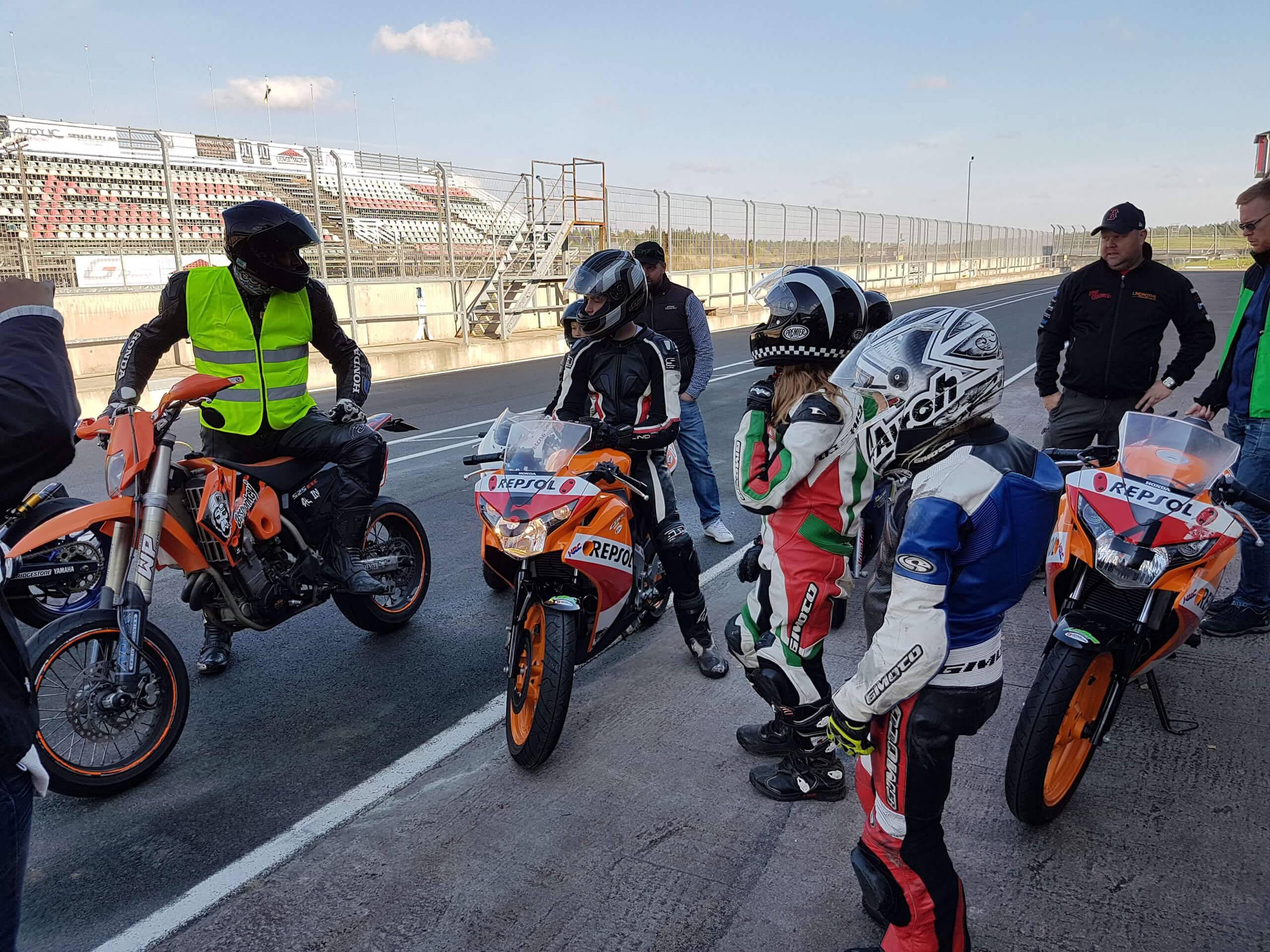 En grupp med nybörjare står och lyssnar på en tränare i roadracing.