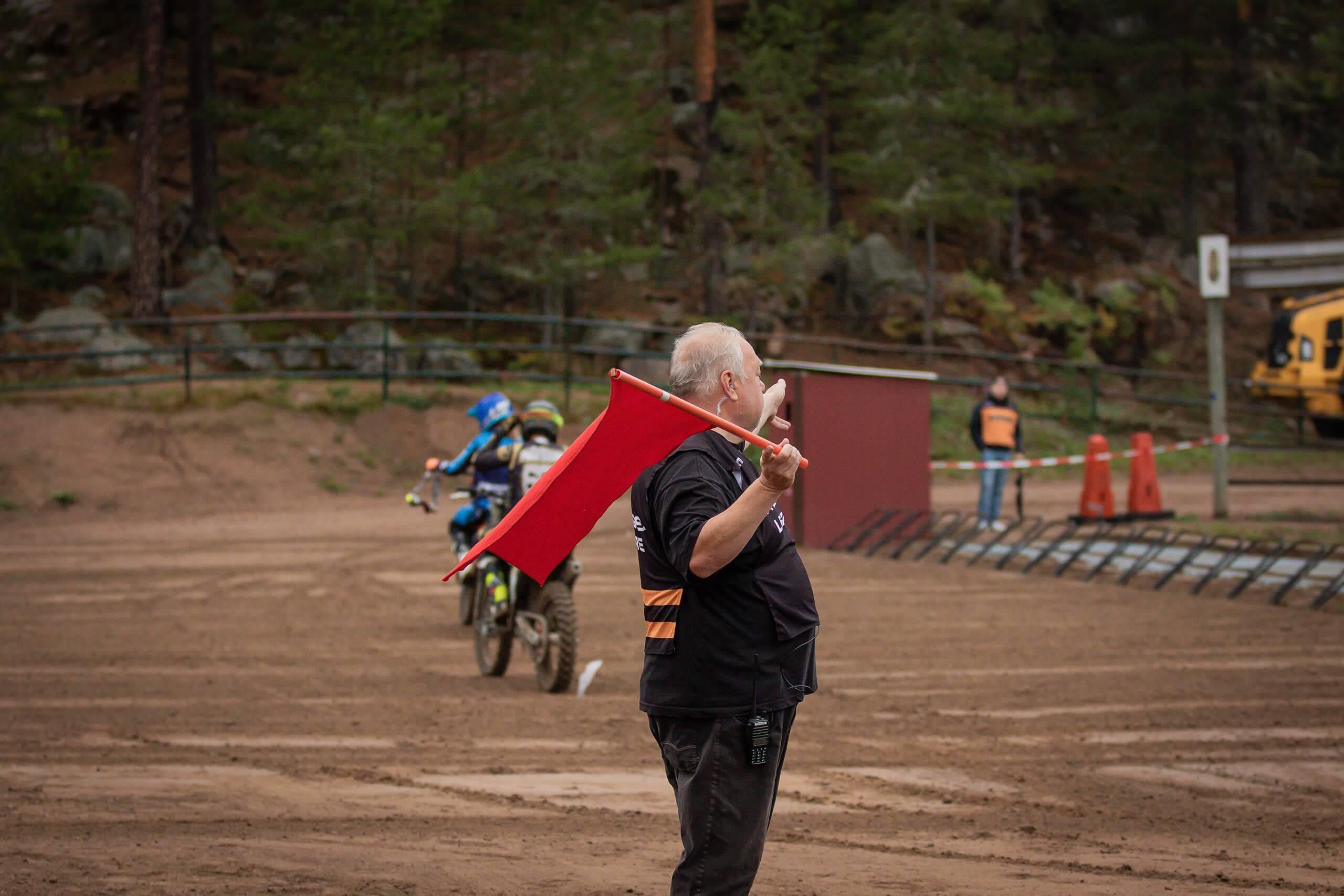 En funktionär visar upp en röd flagga vid startgrindarna på en motocrossbana. Fotograf: Emma Kardestam