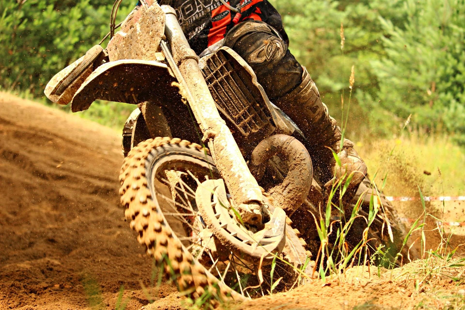 En motocross på en sandig bana och däcket sprätter upp grus.