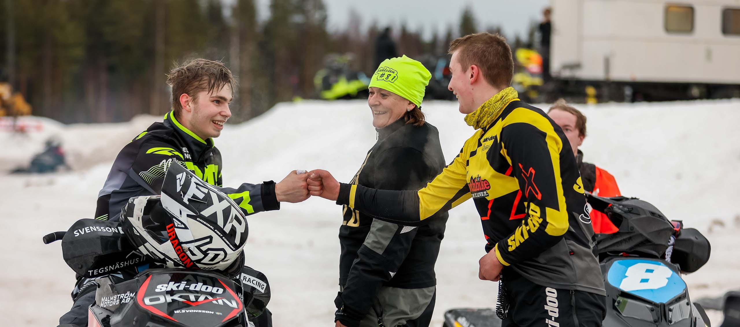 Två snöskoterförare skrattar och slår ihop sina knytna nävar med varandra
