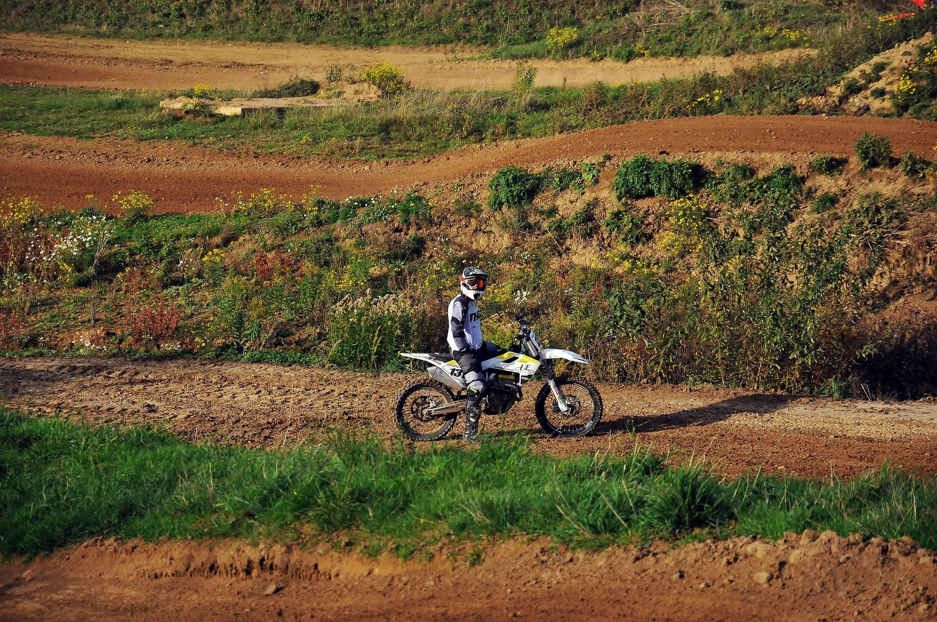 En motocrossförare står stilla med motocrossen på en banan omgiven av grönska och blommor