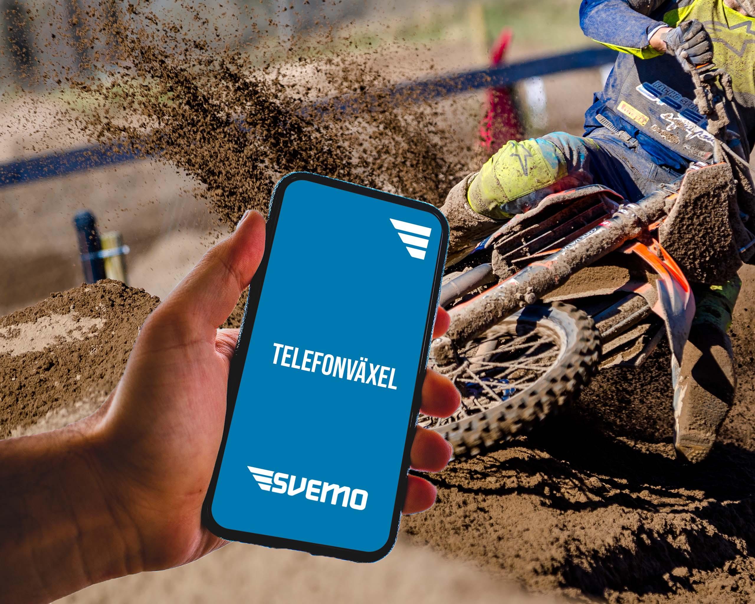 En hand som håller i en telefon framför en crossbana. På telefonens skärm står det Telefonväxel.