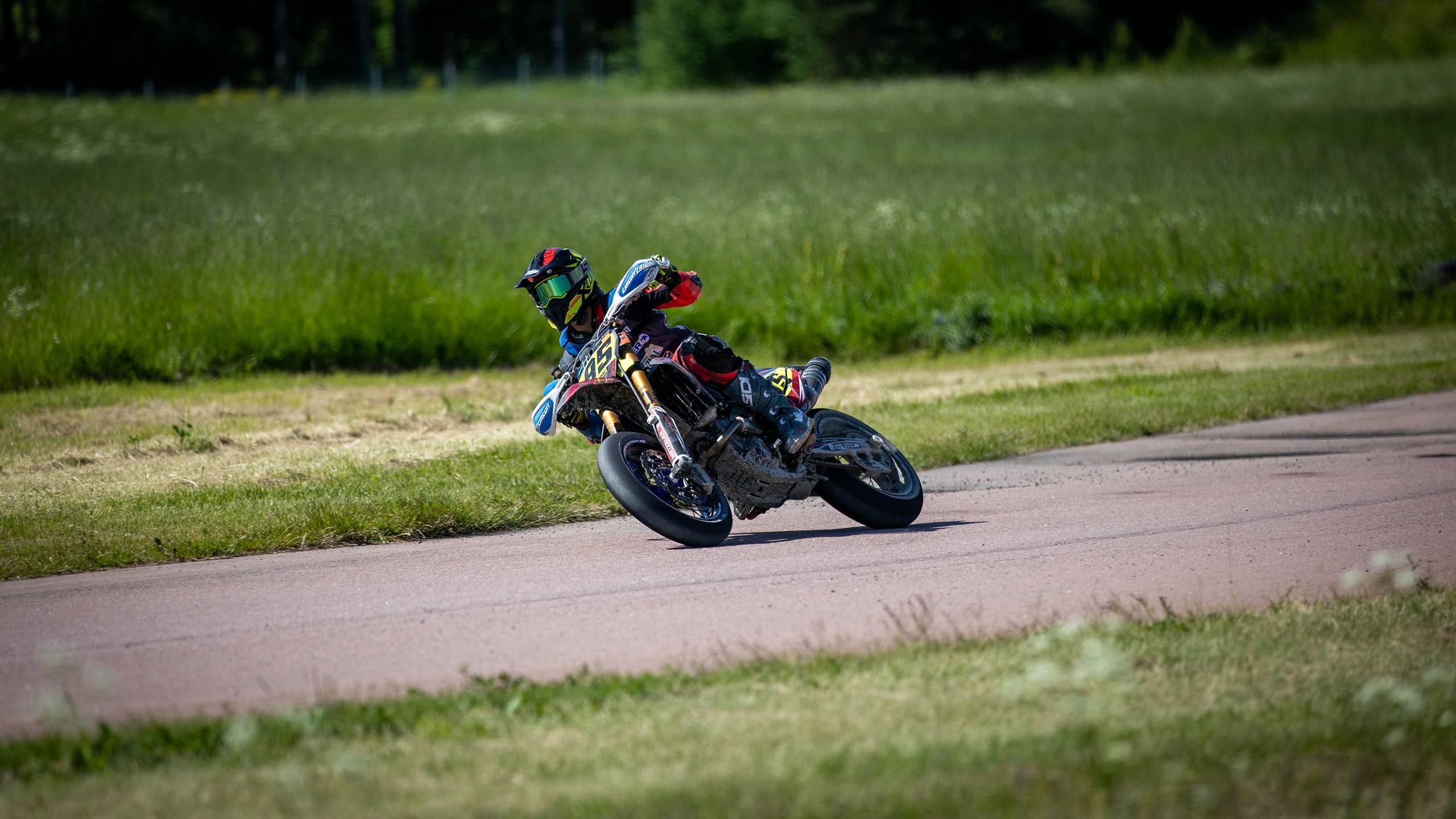 En supermotoförare på sin motorcykel på en väg mellan två gröna gräsfält. Fotograf: Maeva Sponbergs