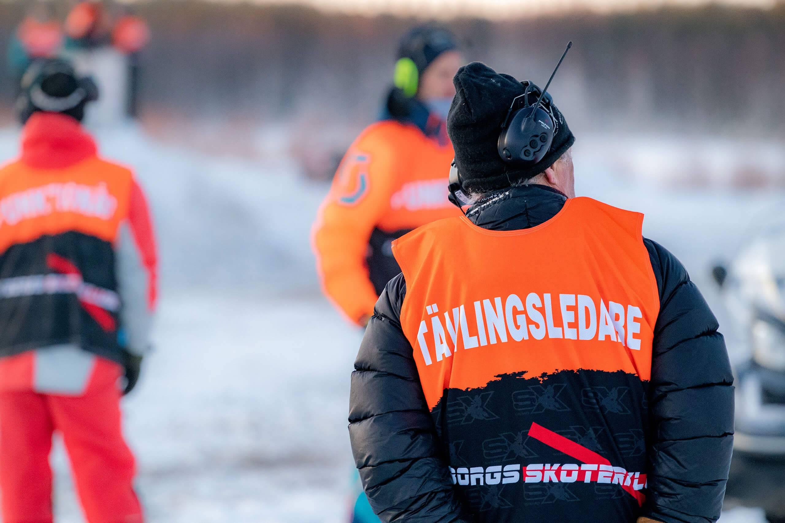En tävlingsledare inom snöskoter i en orange funktionärsväst med texten tävlingsledare på ryggen