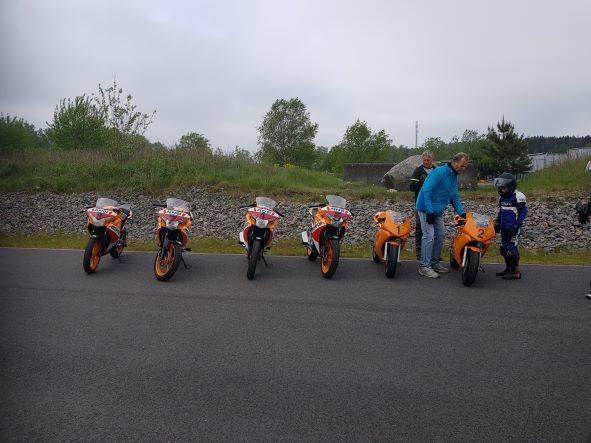 Sex orangea motorcyklar står uppradade bredvid varandra. Två vuxna och ett barn står vid den ena motorcykeln.