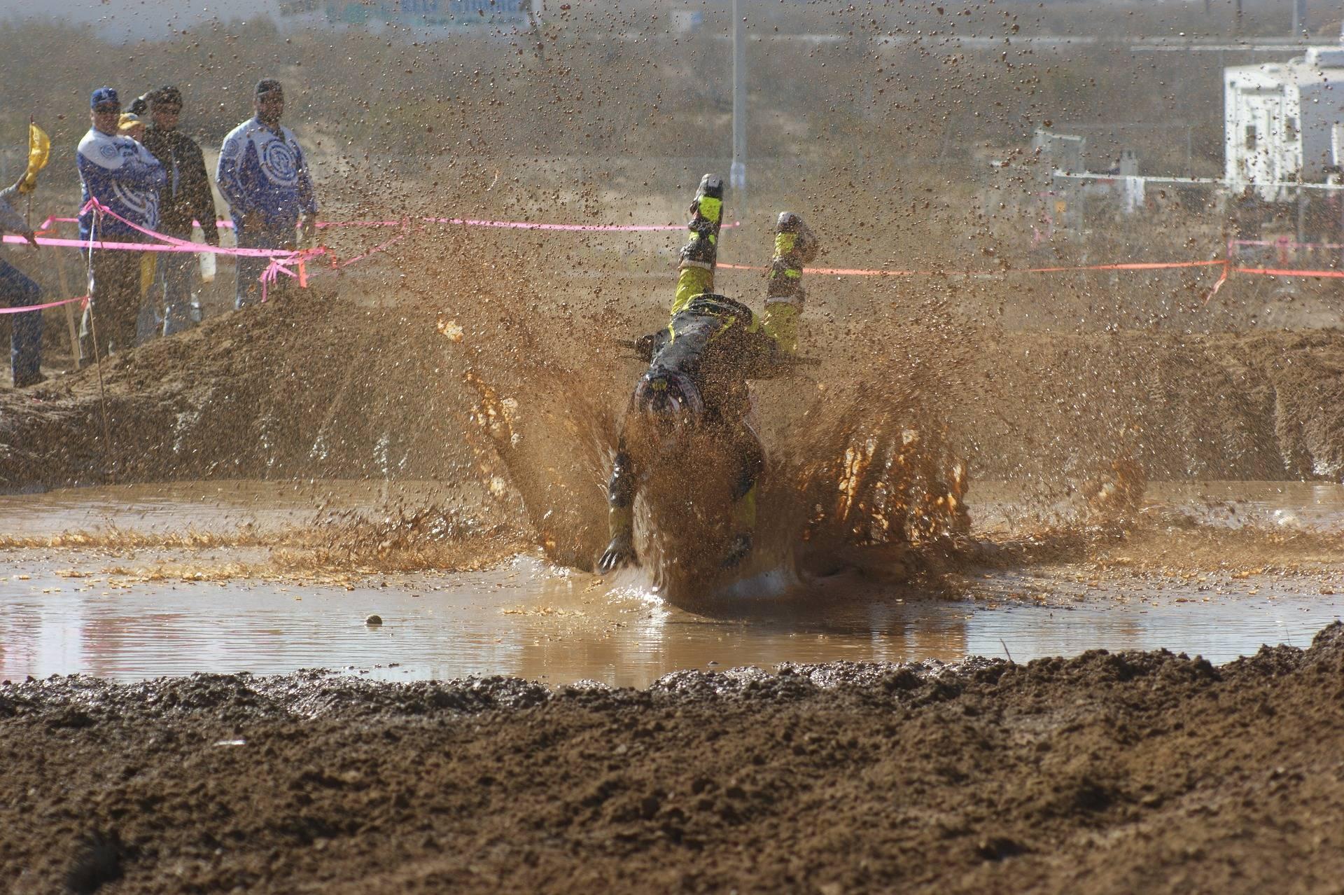 En motocrossförare faller framlänges över styret och ner i leran
