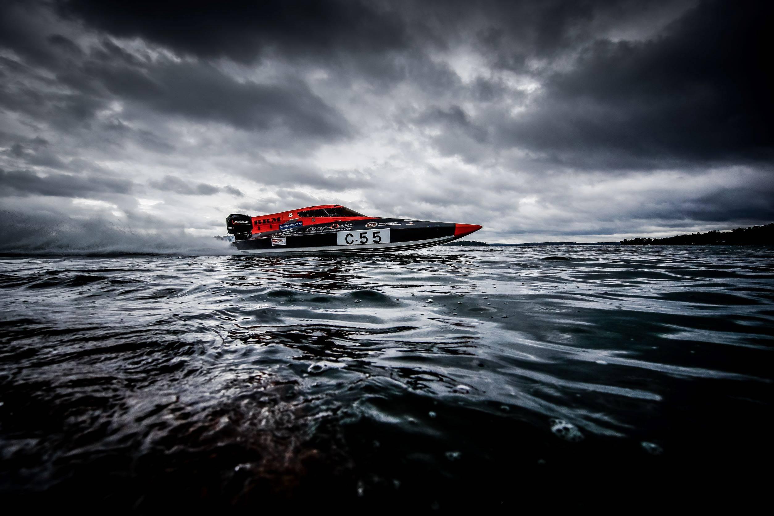 En svart och röd offshore-båt glider fram över mörkt vatten under en himmel täckt av moln.