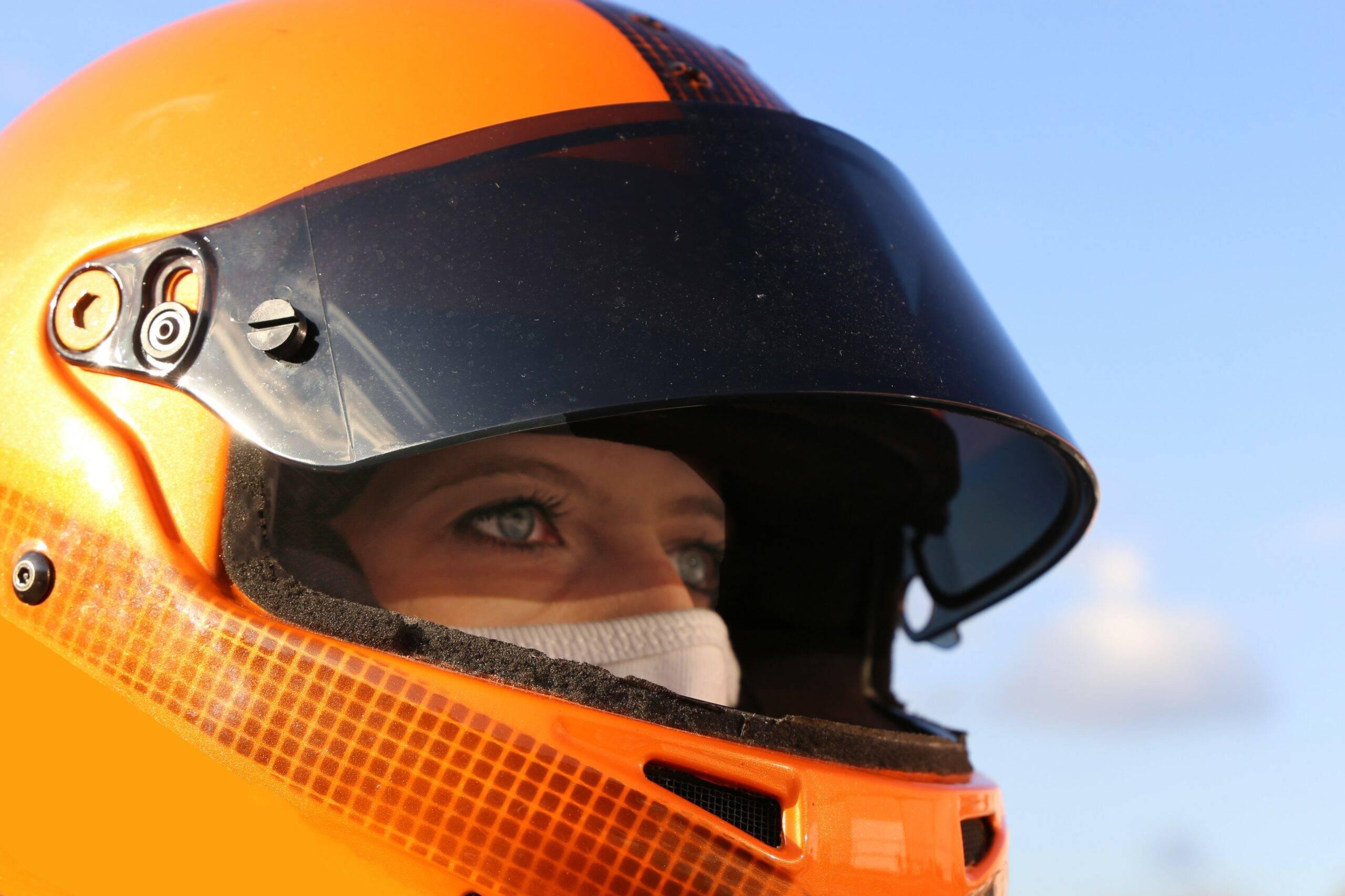 En kvinna med en orange motorcykelhjälm tittar på något i fjärran.