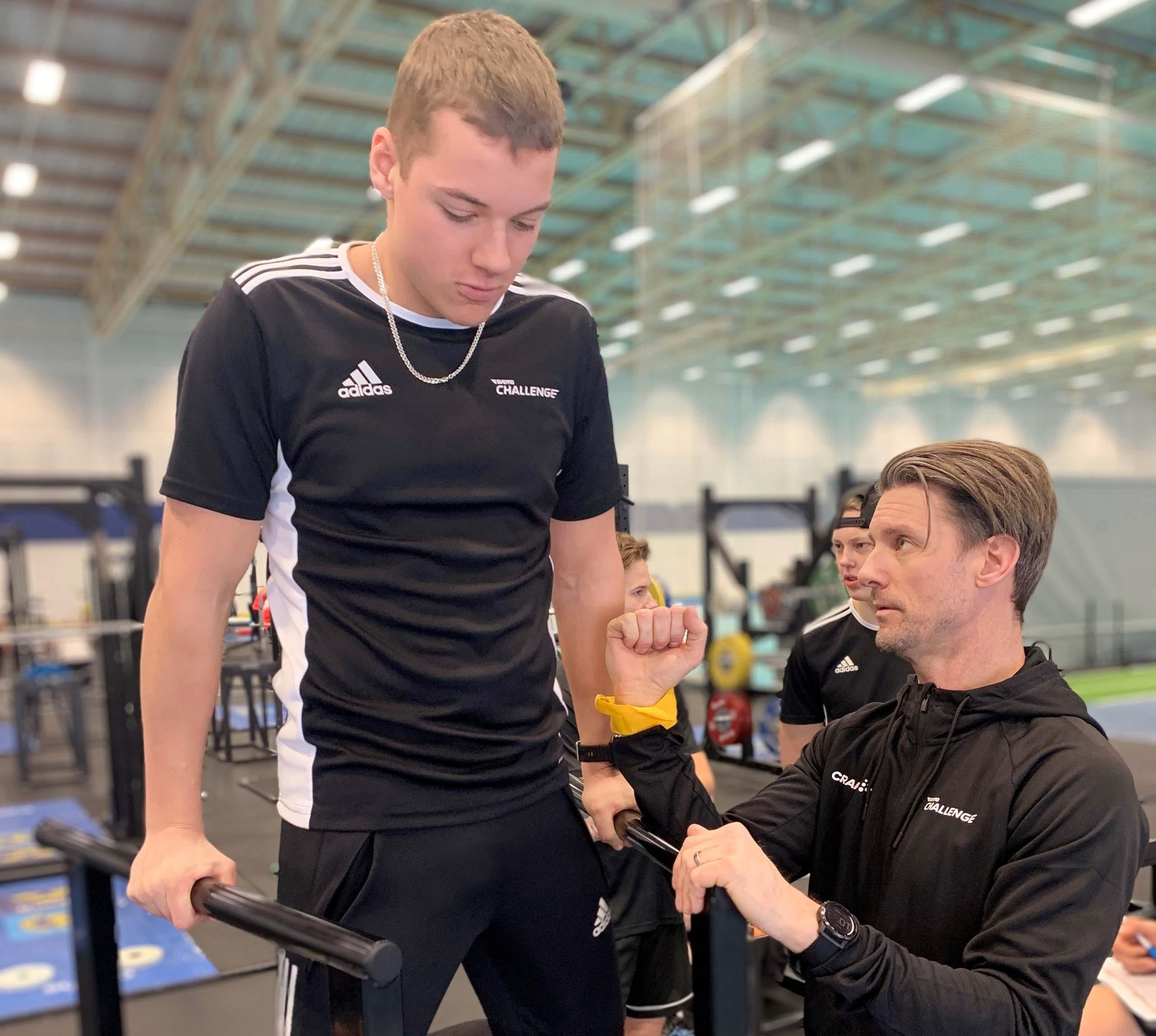 En elev på Svemo Challenge gör dips på en dip bar och får instruktioner från en tränare.