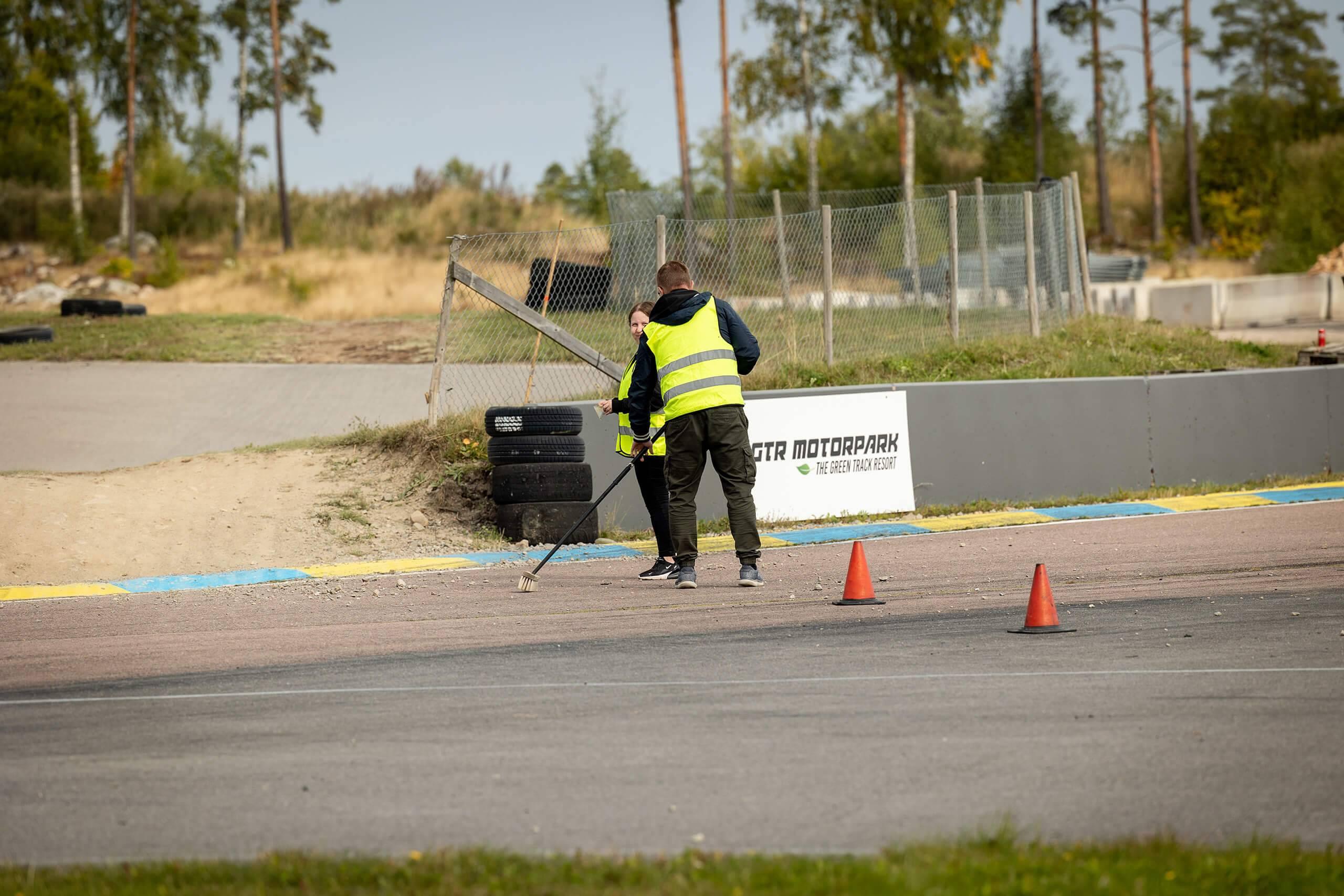 Två funktionärer soppar bort grud från en asfaltsbana. Fotograf: Maeva Sponbergs