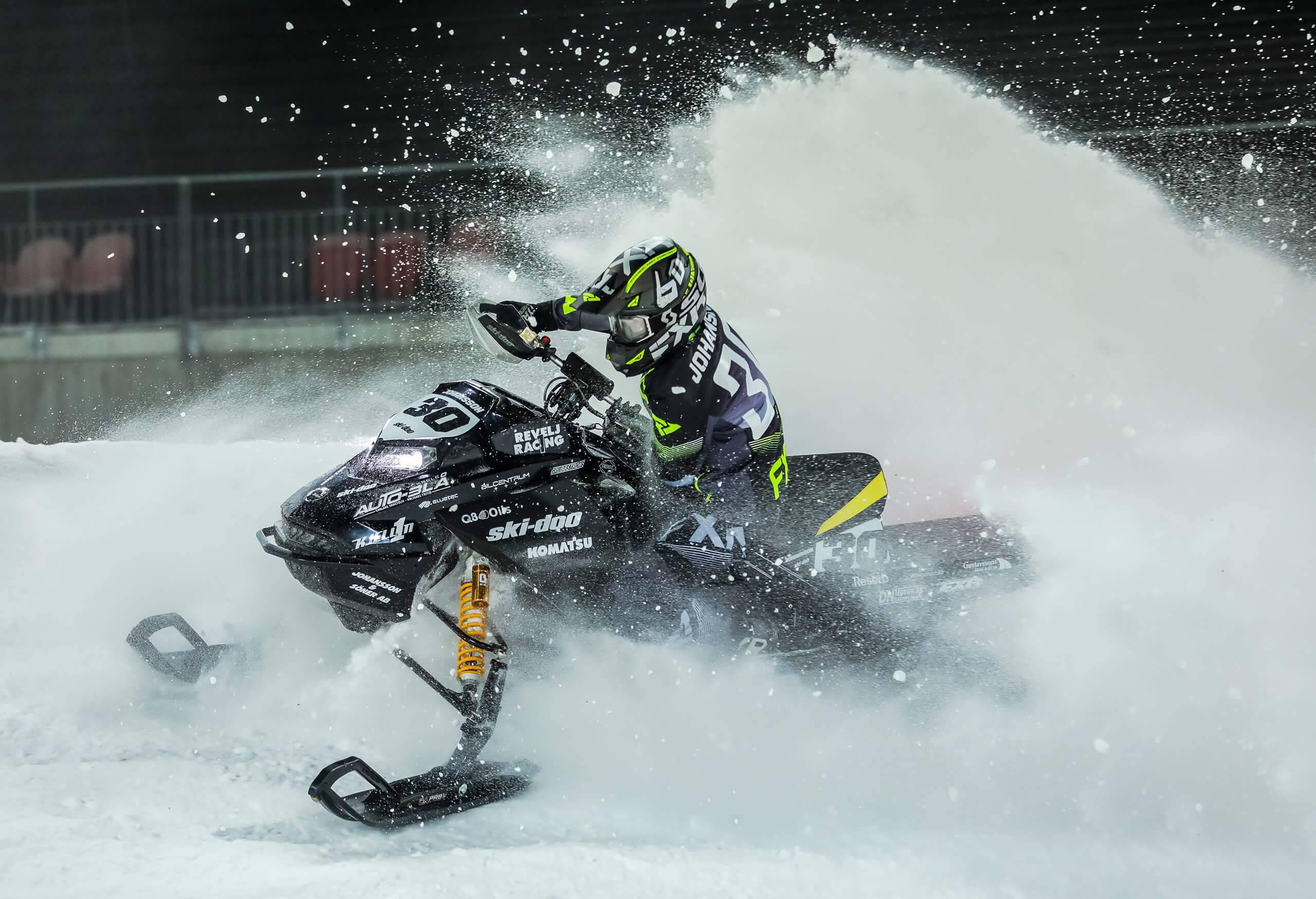 Snöskoterförare mitt i snösprutet som omger skotern