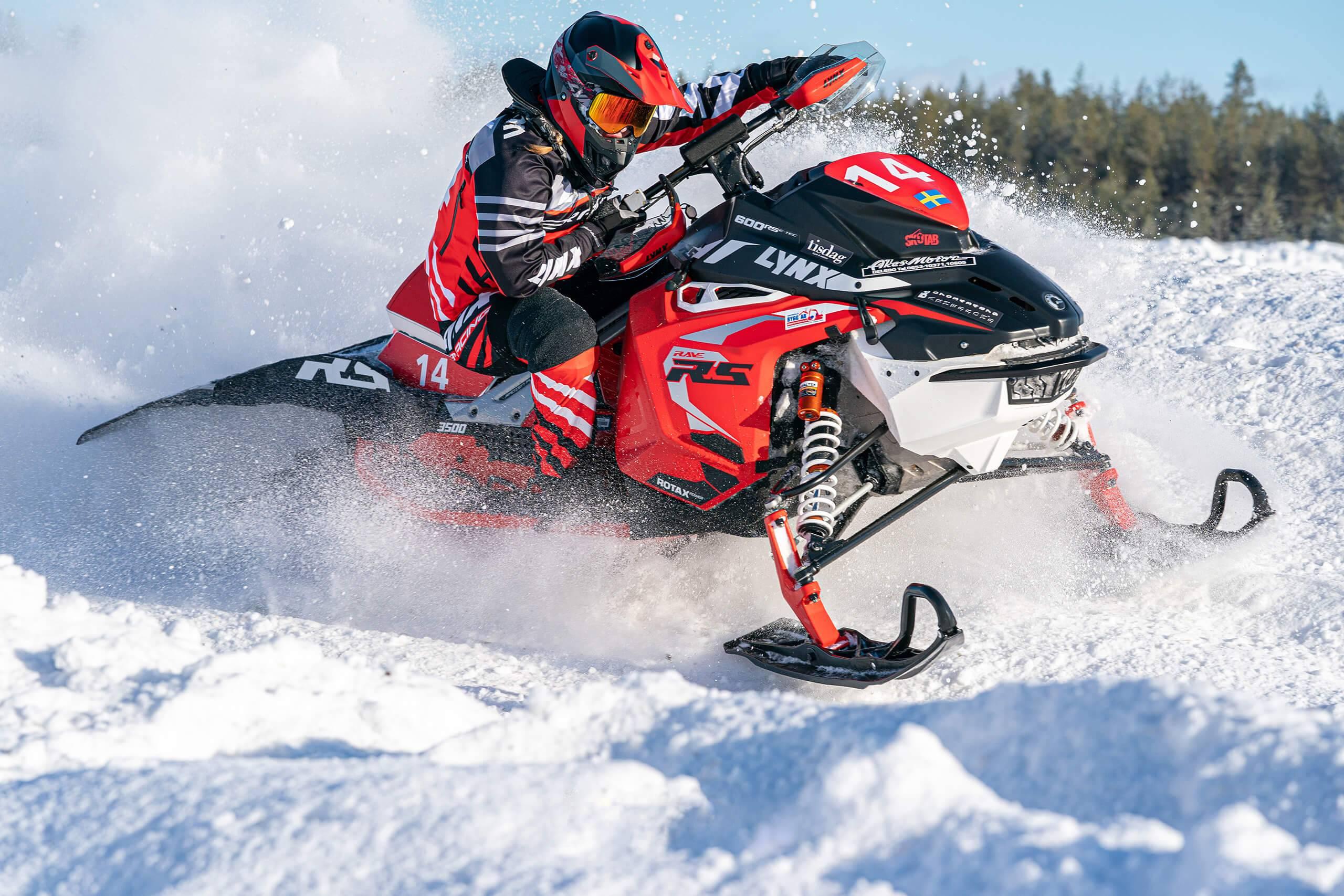 En snöskoterförare manövrerar sin skoter ur en skarp kurva så att snön yrar