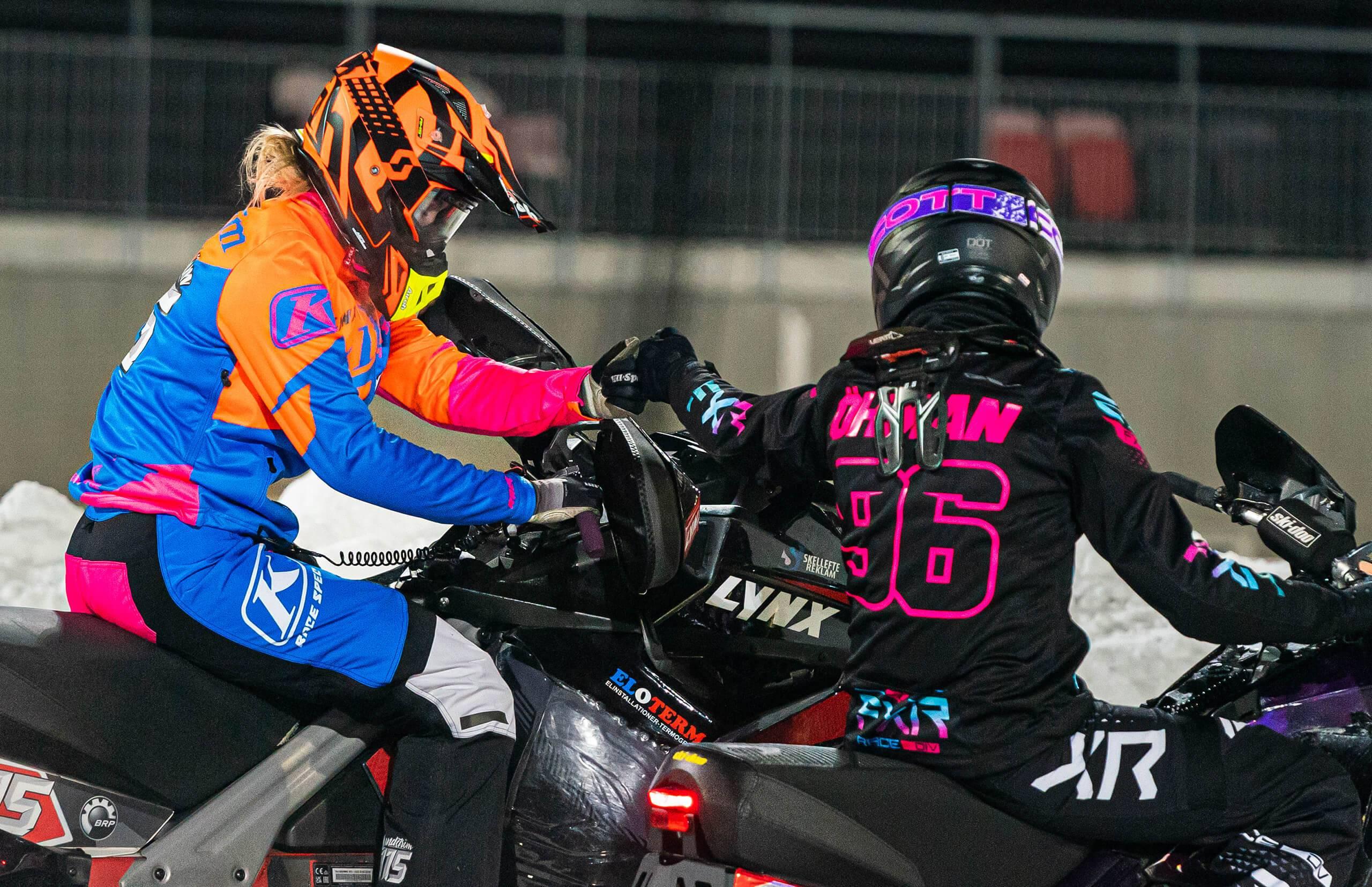 Två kvinnliga snöskoterförare dunkar nävarna med varandra inför eller efter en tävling