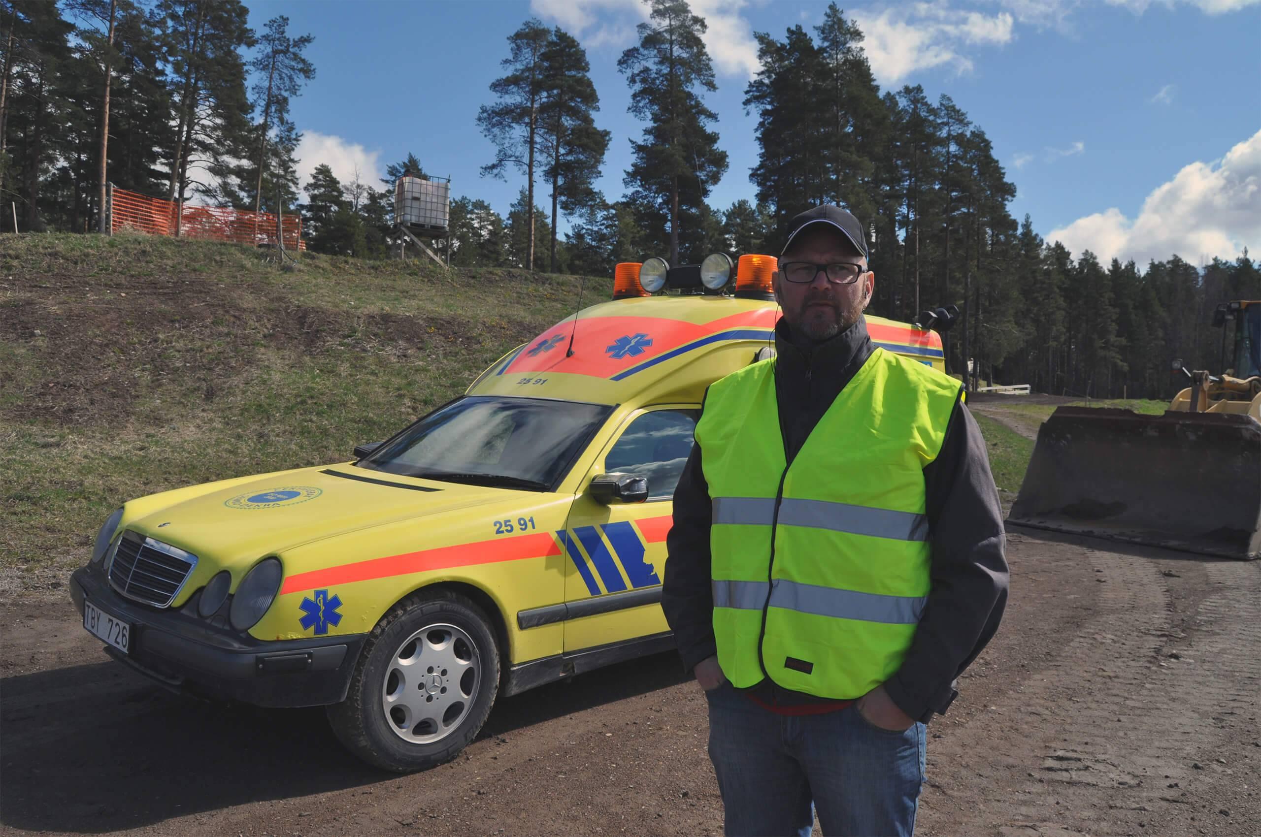 En funktionär i reflexväst står framför en ambulans
