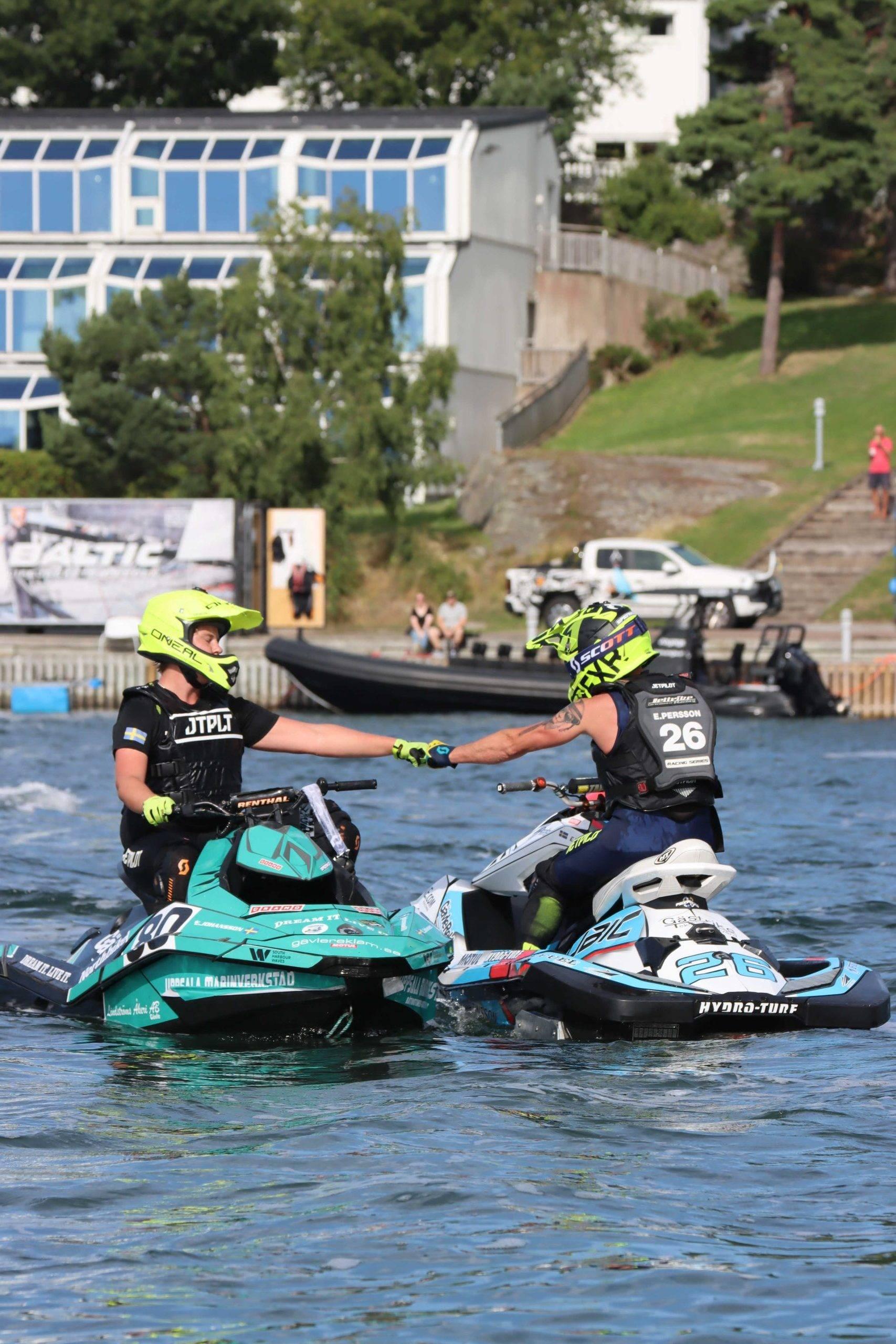 Två vattenskoterförare sträcker ut var sin hand till varandra