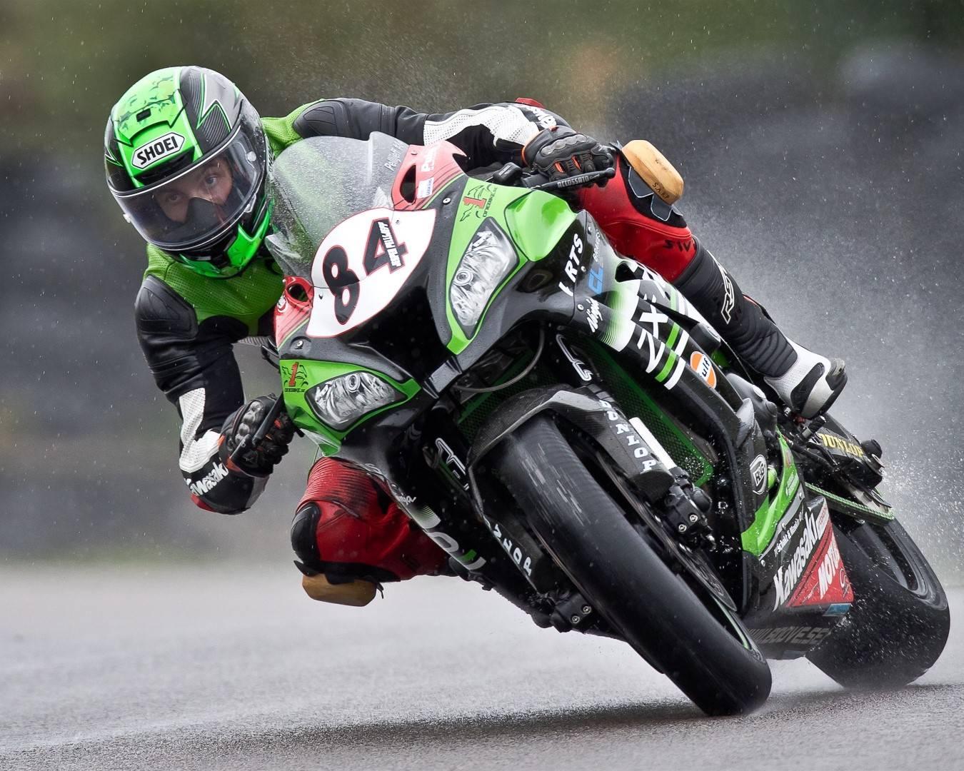 En förare flyger fram över banan på sin roadracing-mc så att vattnet skvätter upp under sig.