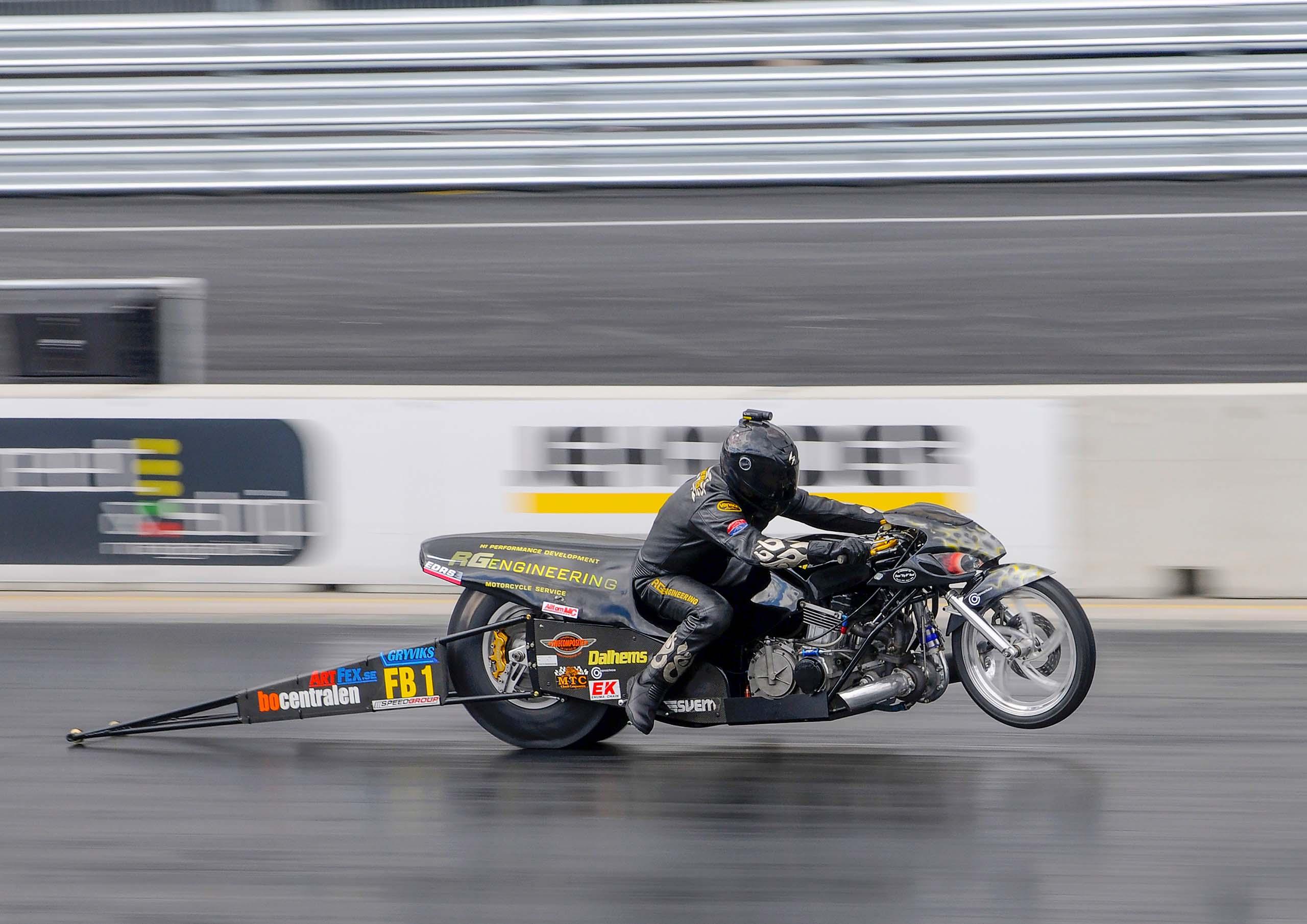 En dragracingförare i full fart framåt. Framdäcket har lyft från marken.