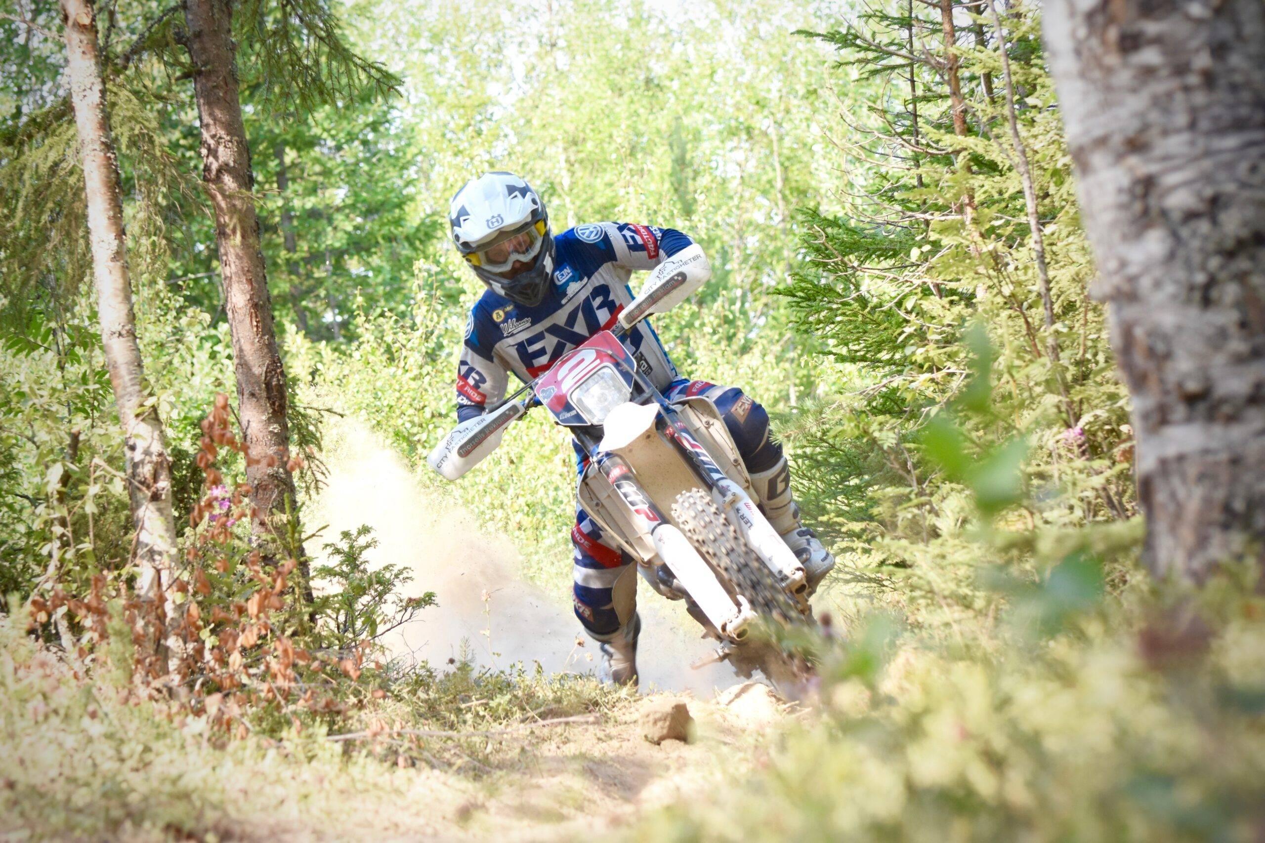 En enduroförare på sin enduro i en grön och somrig skog.