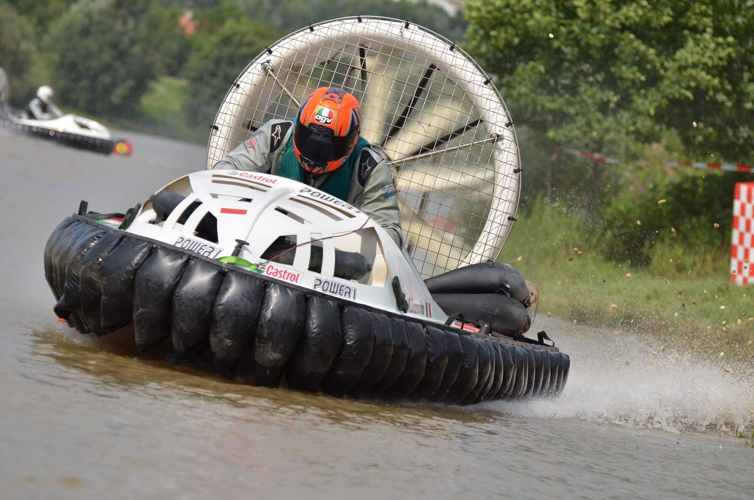 En förare med orange hjälm i en svävare på vattnet. Bakom så sprutar vattnet.