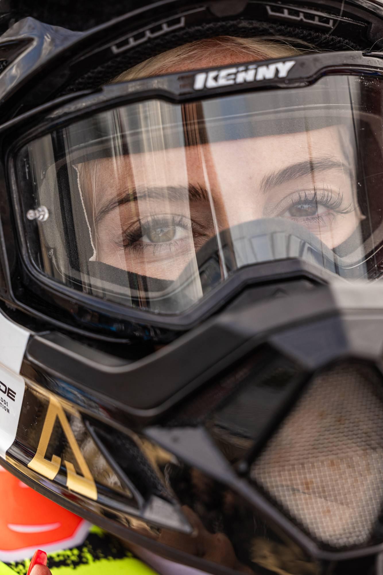 Närbild på en kvinna iklädd skyddshjälm för motorsport samt skyddsglasögon. Hon stirrar med en intensiv och koncentrerad blick in i kameran.