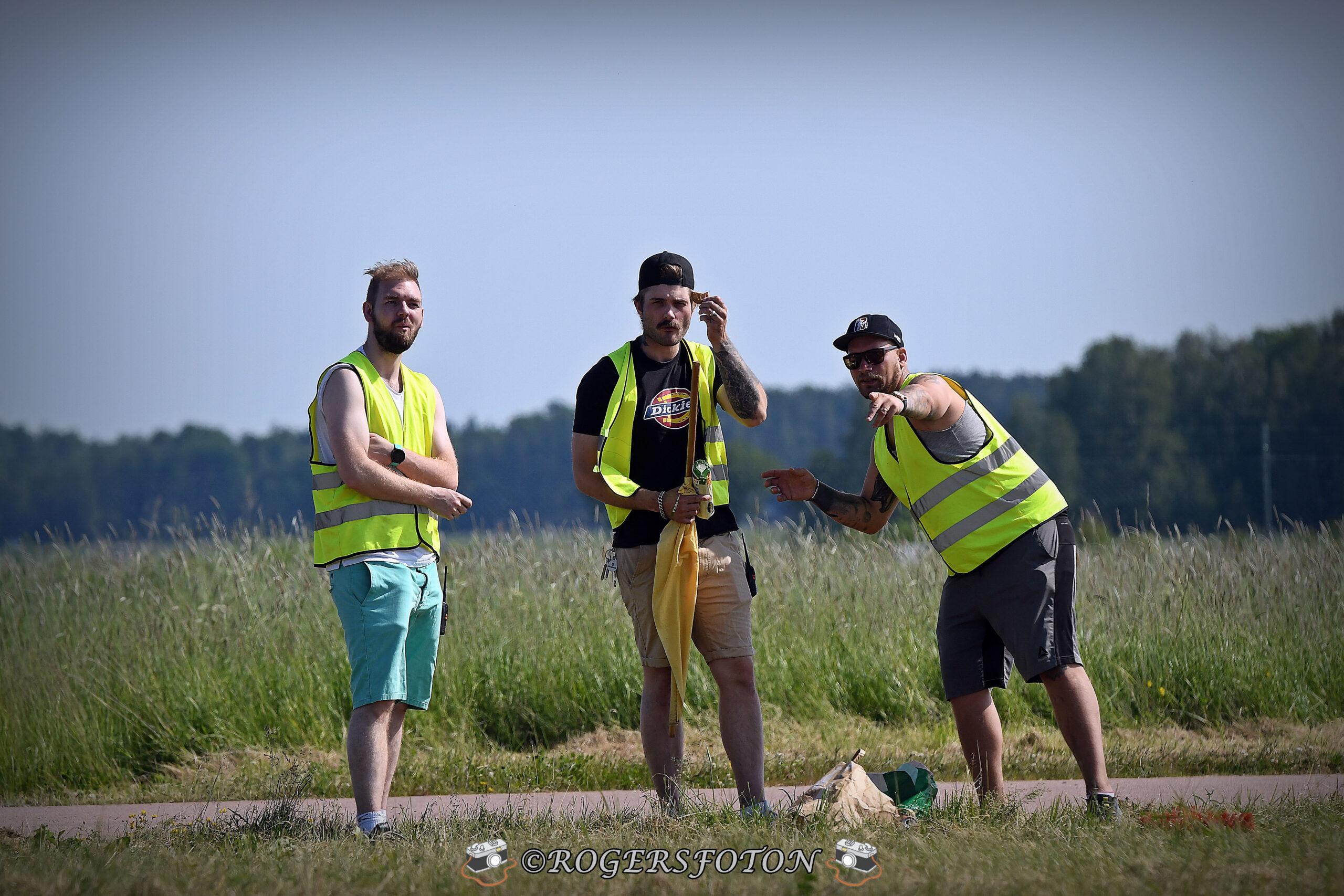 Tre funktionärer i varselvästar står på sidan av en motorsportbana och diskuterar med varandra